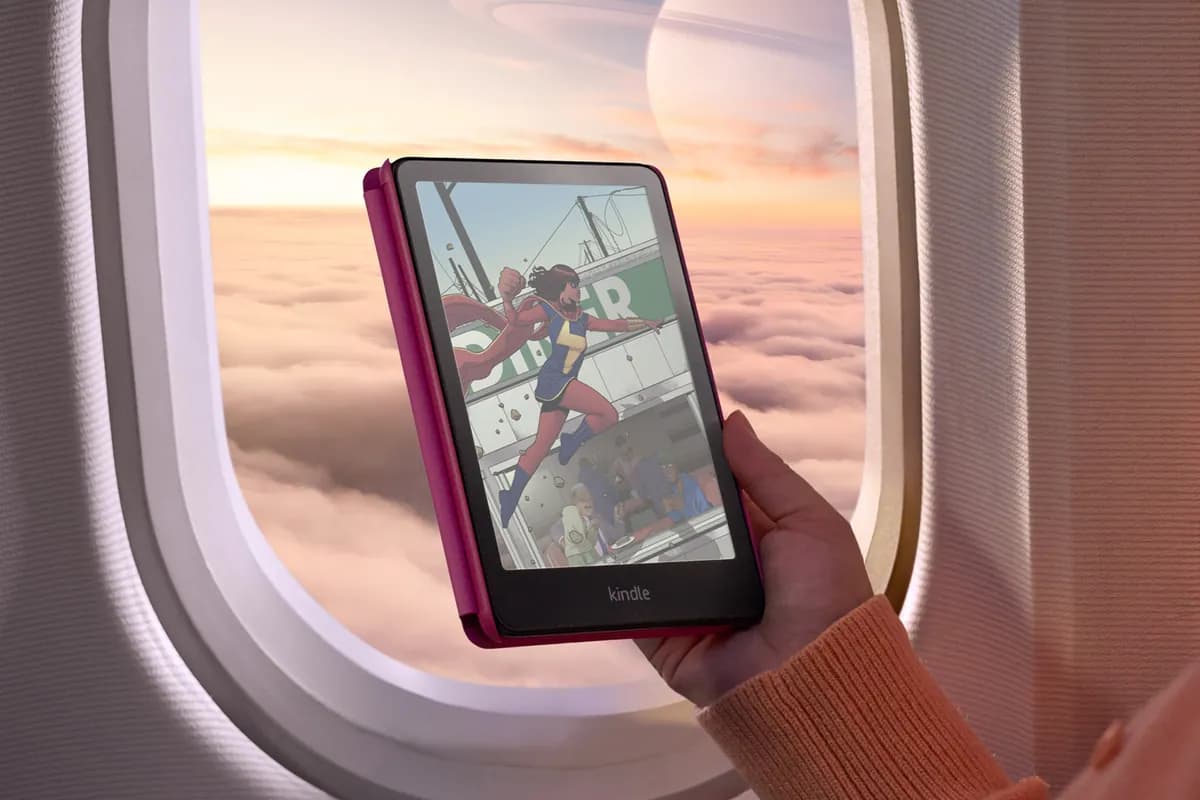 A Kindle Colorsoft showing a color comic page, held up to an airplane window at sunset
