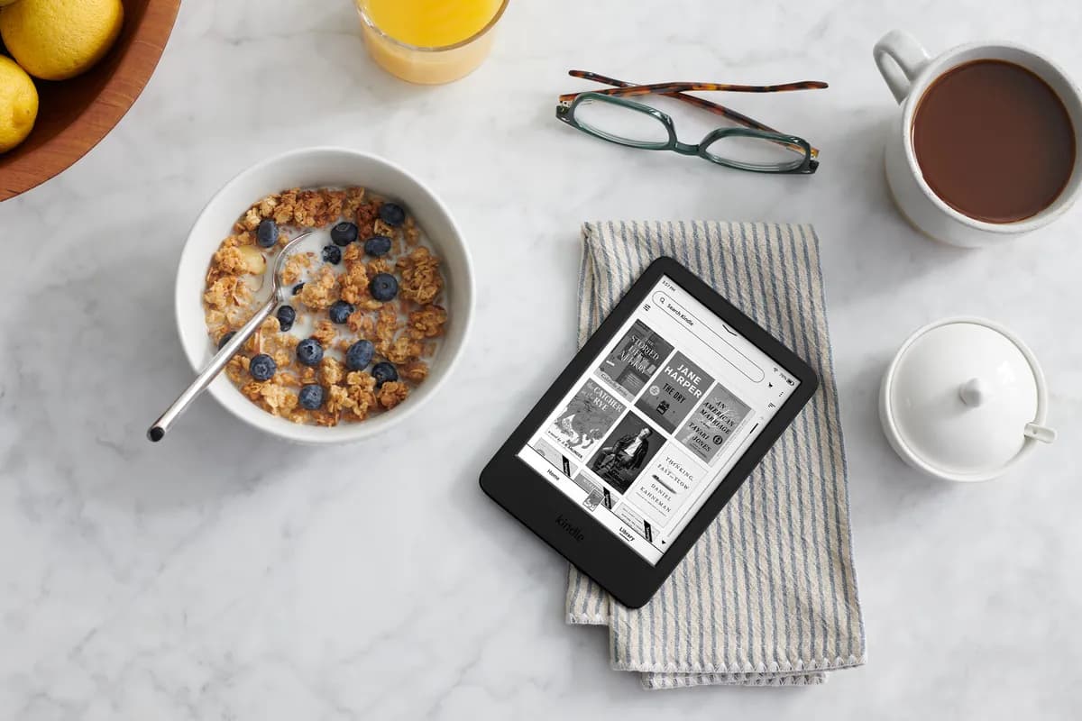 The basic Kindle lying on a breakfast table beside a bowl of cereal and a cup of cocoa