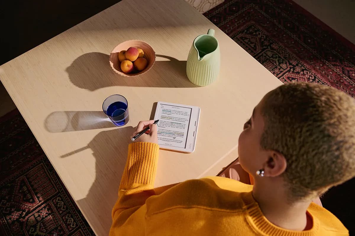 A reader at a sunny table marking up a Kobo Libra Colour with the Kobo stylus