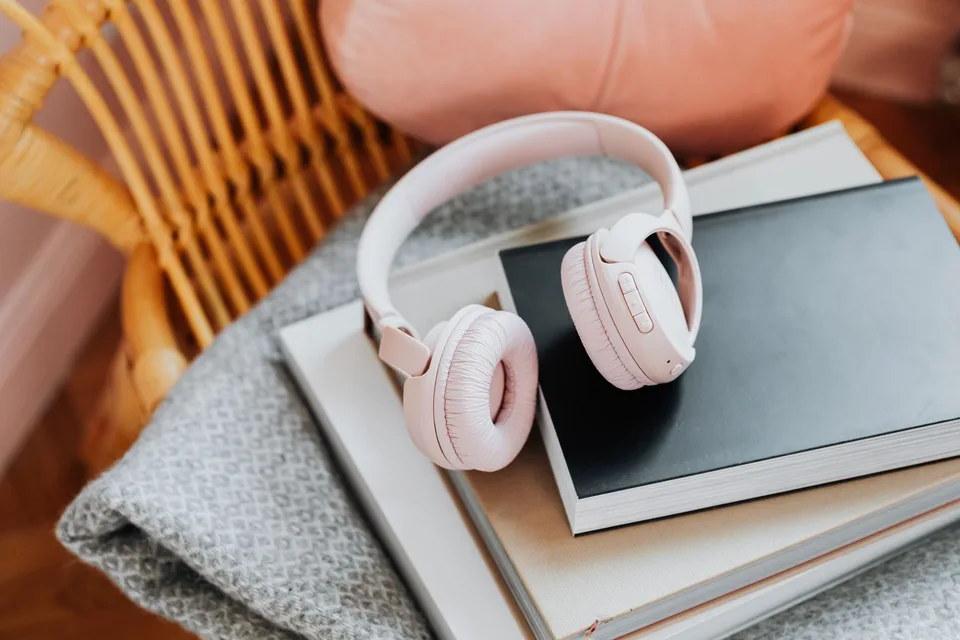 Pink wireless headphones on a stack of books on a rattan chair