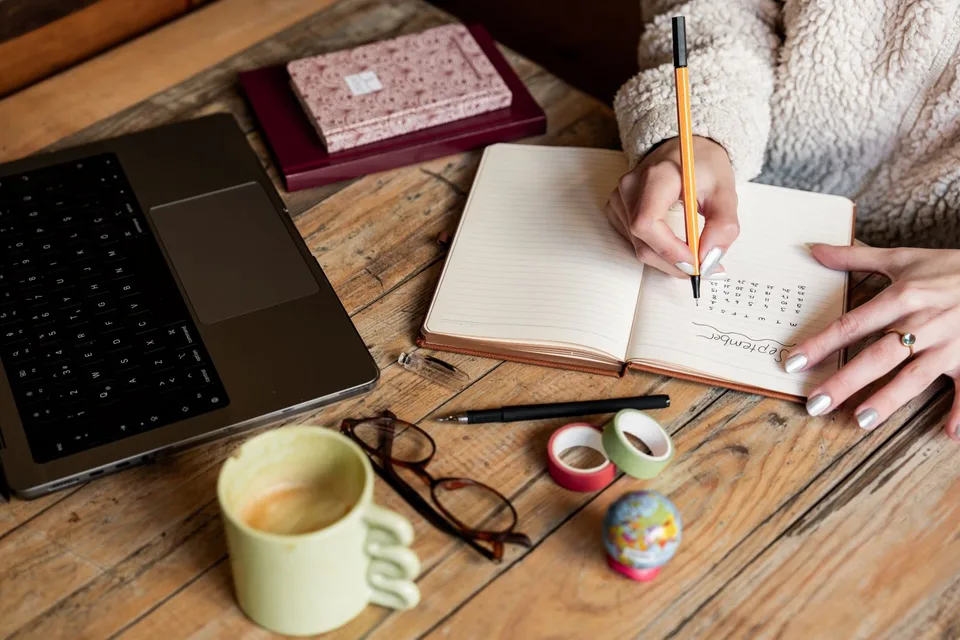 An author planning a book marketing campaign in a notebook beside a laptop and coffee on a bright desk
