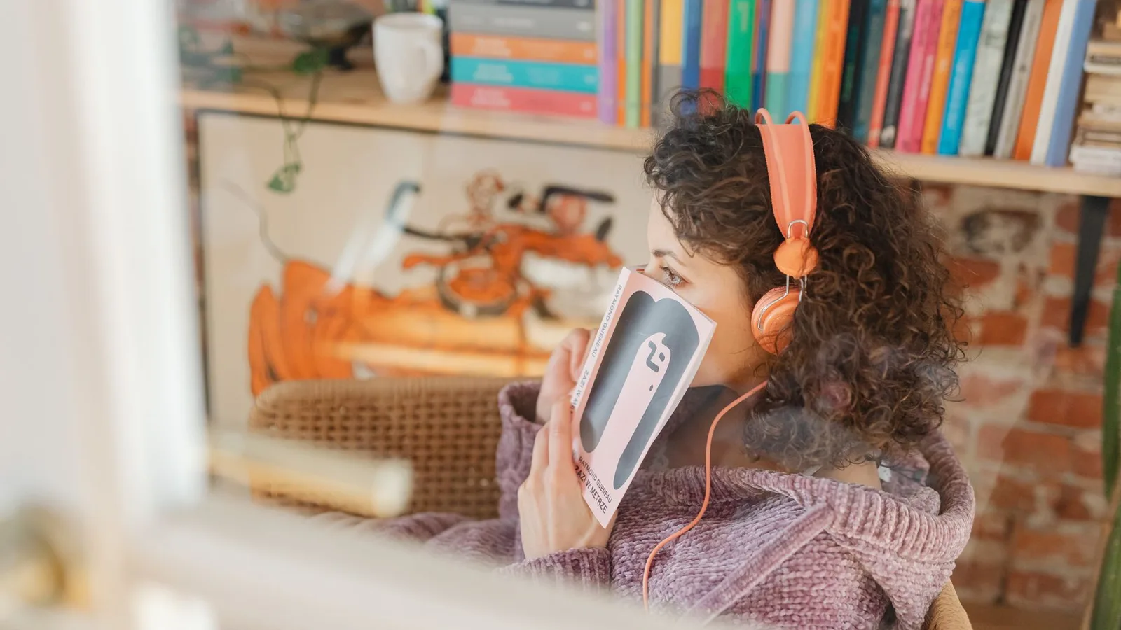 A woman in headphones listening to a book beside a wall of bookshelves