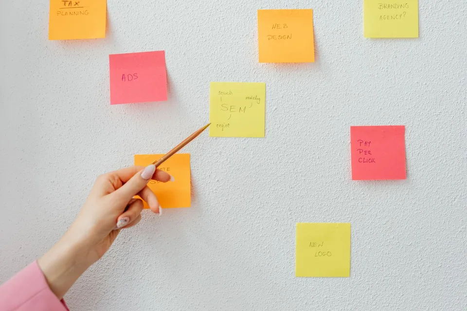 A writer planning a novel by arranging and pointing at sticky notes on a wall, mapping scenes before drafting